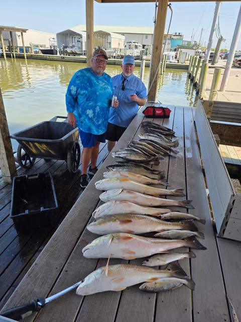Two men with a large catch of fish on a wooden dock next to water.