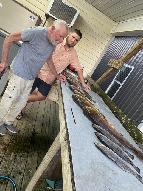 Two men inspecting fish laid out on a table on a dock.