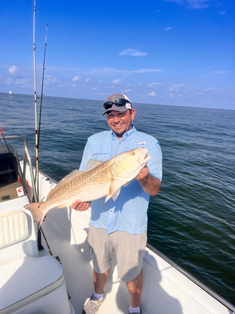 Man on a boat holding a large redfish he caught on a sunny day.