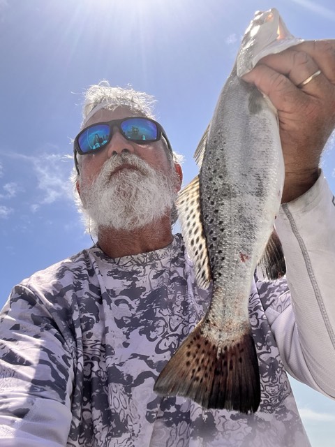 Man holding speckled trout, blue sky background.