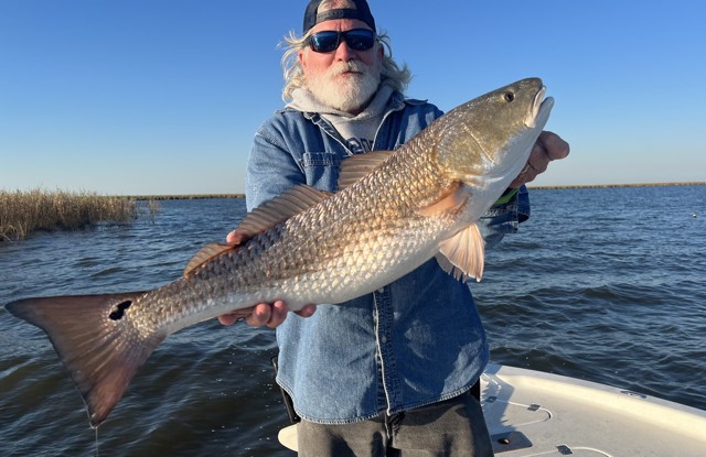 Man holding a large redfish on a boat; blue water and sky background.