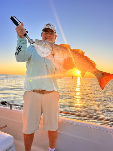 Man on a boat holding a large redfish at sunset.