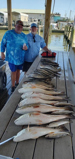 Two men stand beside a table covered with fish on a dock.